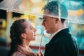 Young beautiful couple spending time together on date in amusement park at night. Rainy weather, autumn. Lovers standing Royalty Free Stock Photo