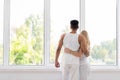 Young Beautiful Couple Stand Near Big Window Embrace, Happy Smile Hispanic Man And Woman Lovers Hug