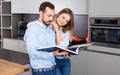 Young beautiful couple standing with book in modern kitchen interior