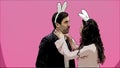 Young beautiful couple standing on a pink background. During this, they are dressed in rabble ears. Looking gently at