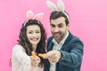 Young beautiful couple standing on a pink background. During this man and his wife hold small isolated carrots in their