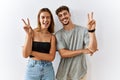 Young beautiful couple standing together over isolated background smiling with happy face winking at the camera doing victory sign Royalty Free Stock Photo