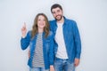 Young beautiful couple standing together over white isolated background showing and pointing up with finger number one while Royalty Free Stock Photo