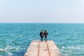 Young beautiful couple in love stands with their backs on a concrete pier and enjoy a beautiful sea view