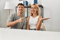 Young beautiful couple wearing casual clothes sitting on the table at home amazed and smiling to the camera while presenting with Royalty Free Stock Photo