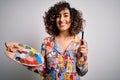 Young beautiful curly arab artist woman painting using brush and palette with colors with a happy face standing and smiling with a Royalty Free Stock Photo