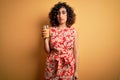 Young beautiful curly arab woman drinking glass of healthy orange juice over yellow background with a confident expression on Royalty Free Stock Photo