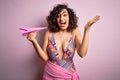 Young beautiful curly arab woman on vacation wearing swimsuit holding pink paper airplane very happy and excited, winner Royalty Free Stock Photo