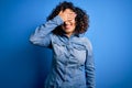 Young beautiful curly arab woman wearing casual denim shirt standing over blue background smiling and laughing with hand on face Royalty Free Stock Photo