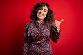 Young beautiful curly arab woman wearing casual floral dress standing over red background smiling with happy face looking and Royalty Free Stock Photo