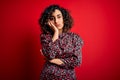 Young beautiful curly arab woman wearing casual floral dress standing over red background thinking looking tired and bored with Royalty Free Stock Photo