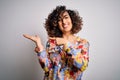 Young beautiful curly arab woman wearing floral colorful shirt standing over white background amazed and smiling to the camera Royalty Free Stock Photo