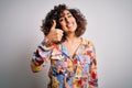Young beautiful curly arab woman wearing floral colorful shirt standing over white background doing happy thumbs up gesture with Royalty Free Stock Photo