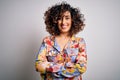 Young beautiful curly arab woman wearing floral colorful shirt standing over white background happy face smiling with crossed arms Royalty Free Stock Photo