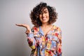 Young beautiful curly arab woman wearing floral colorful shirt standing over white background smiling cheerful presenting and Royalty Free Stock Photo