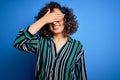 Young beautiful curly arab woman wearing striped shirt and glasses over blue background smiling and laughing with hand on face Royalty Free Stock Photo