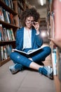 Young beautiful curly girl in glasses and blue suit sitting with books in the library. Royalty Free Stock Photo