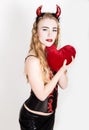 Young and beautiful curly girl with red horns looks like pretty Devil, holding a heart pillow Royalty Free Stock Photo