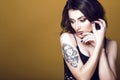 Young beautiful dark haired tattooed woman wearing black net top, holding her hands at her face and looking down thoughtfully