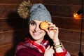 Young beautiful dark-haired woman smiling in winter clothes and cap with tangerines on wooden background.