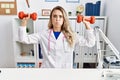 Young beautiful doctor woman holding dumbbells for sport therapy puffing cheeks with funny face Royalty Free Stock Photo