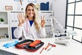 Young beautiful doctor woman with reflex hammer and medical instruments showing and pointing up with fingers number seven while Royalty Free Stock Photo