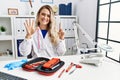 Young beautiful doctor woman with reflex hammer and medical instruments showing and pointing up with fingers number six while Royalty Free Stock Photo