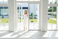 A young beautiful elegant woman enters the open door of a house with huge high panoramic windows to the floor