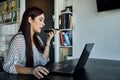 Young, beautiful and empowered female entrepreneur, talking on a smartphone on speakerphone while working on her laptop in the Royalty Free Stock Photo