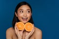 Young beautiful enthusiastic happy asian woman holding two oranges halves