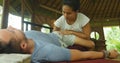 Young beautiful and exotic Asian Indonesian therapist woman giving traditional Thai massage to man relaxed at tropical wellness