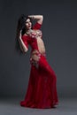 Young beautiful exotic eastern women performs belly dance in ethnic red dress on gray background Royalty Free Stock Photo