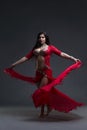 Young beautiful exotic eastern women performs belly dance in ethnic red dress on gray background Royalty Free Stock Photo