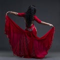 Young beautiful exotic eastern women performs belly dance in ethnic red dress with open back on gray background Royalty Free Stock Photo