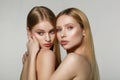 Young beautiful faces of two adult girls with bare shoulders on grey background