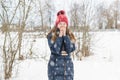 Young beautiful fair-haired girl breathes on her hands in order to warm them in the park under soft fluffy snow