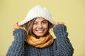 Young beautiful fair-haired girl in knited hat sweater scarf and mittens smiling looking at camera over yellow Royalty Free Stock Photo