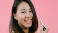 Young beautiful fashionable Asian woman applying lips makeup with cosmetic brush in casual clothing over pink background studio Royalty Free Stock Photo