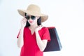 Young beautiful fashionable Asian woman holding shopping bags wearing red dress, sunglasses and hat over white background studio Royalty Free Stock Photo