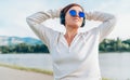 Young beautiful female in blue sunglasses listening to music using smartphone and wireless headphones cheerfully smiling. Walking Royalty Free Stock Photo