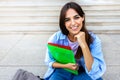 Young beautiful female college student sitting on stairs outside university building looking at camera. Copy space. Royalty Free Stock Photo