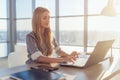 Young beautiful female copywriter typing texts and blogs in spacious light office, her workplace, using pc keyboard