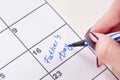 Girl hands with blue felt pen writing words Fathers Day in calendar