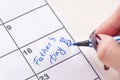 Girl hands with felt pen writes word Father day and drawing tie bow in calendar