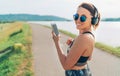 Young beautiful female listening to music using smartphone and wireless headphones and starting jogging and cheerfully smiling in