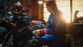 Young Beautiful Female Mechanic is Fixing a Custom Bobber Motorcycle. Talented Girl Wearing a Blue Royalty Free Stock Photo