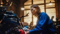 Young Beautiful Female Mechanic is Working on a Custom Bobber Motorcycle. Talented Girl Wearing a Royalty Free Stock Photo