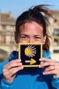 Young beautiful female pilgrim`s portrait posing with the typical `Camino de Santiago` blue tile painted with a yellow shell Royalty Free Stock Photo