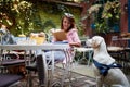 A young beautiful female student is enjoying a company of her dog while reading a book in the bar. Leisure, bar, friendship,