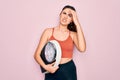 Young beautiful fitness woman wearing sport clothes holding weighting machine scale stressed with hand on head, shocked with shame Royalty Free Stock Photo